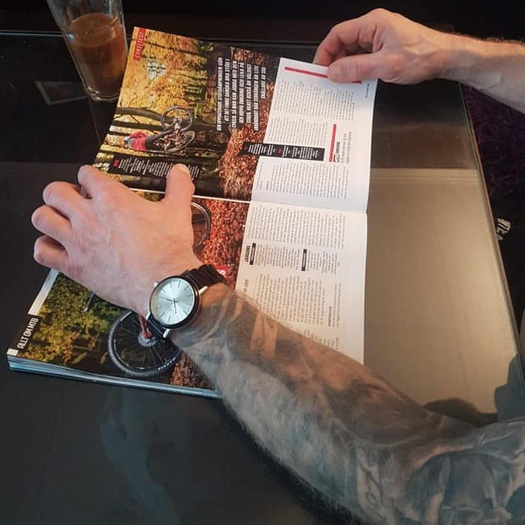 Mycket nöjd kund läser cykeltidning. Svart Ebony på armen. Träklocka från Donum.earth